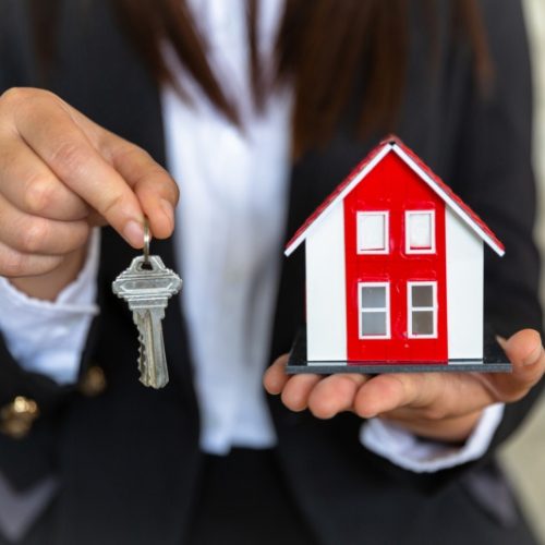 A real estate agent with a key. Red roof house. Offering home, property insurance, and housing safety concepts. Choosing a house in the future. Banking and home mortgages. (A real estate agent with a key. Red roof house. Offering home, property insura